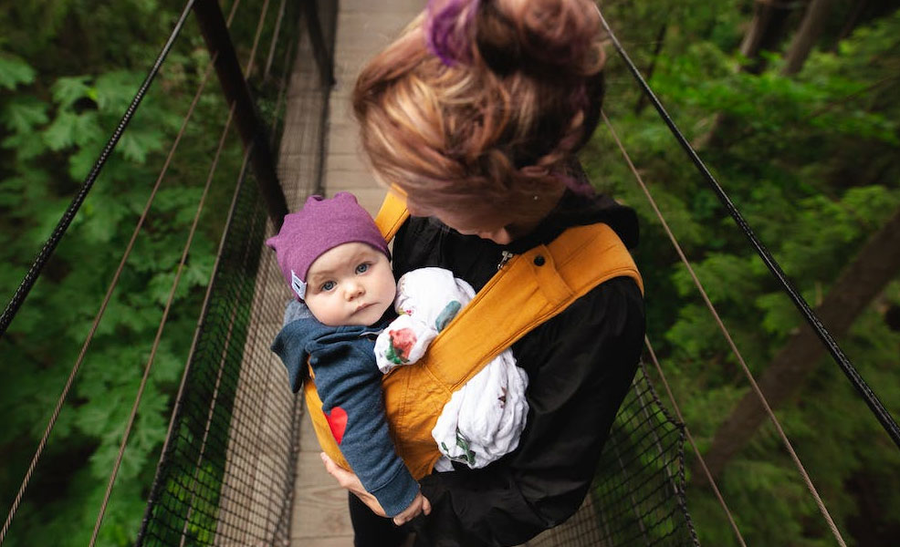 mother carrying baby in a carrier while crossing a bridge while hiking