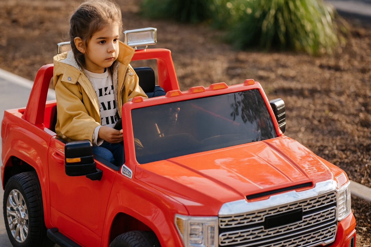 girl driving a red power wheels ride-on toy on sidewalk